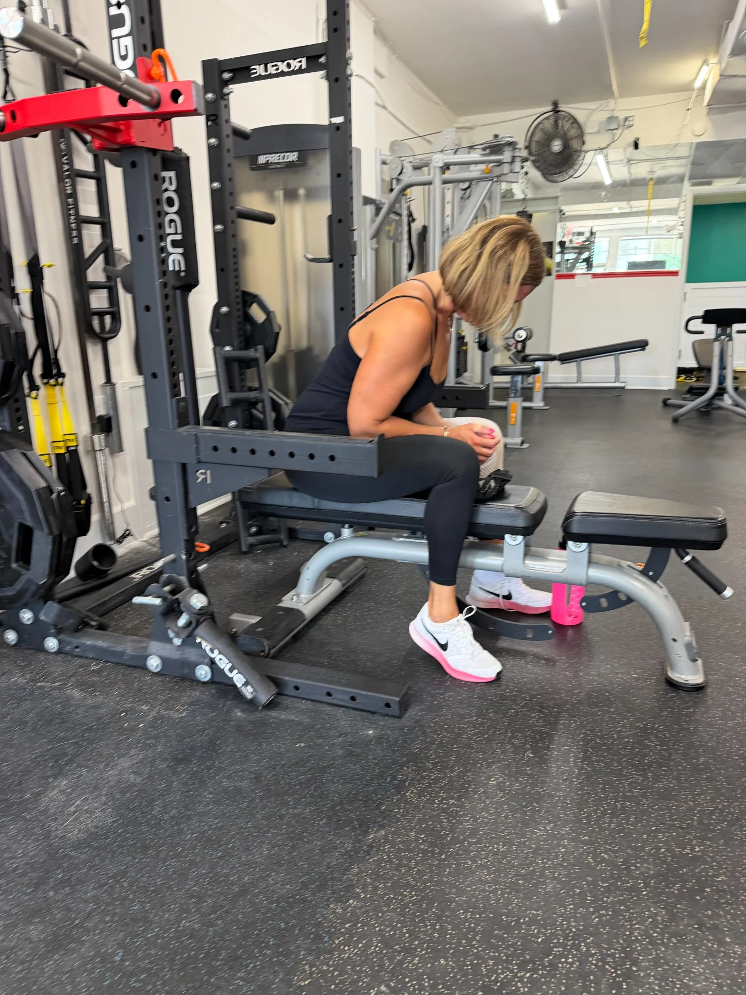Woman seated on a bench inside a squat rack between sets at The Gym Connection.