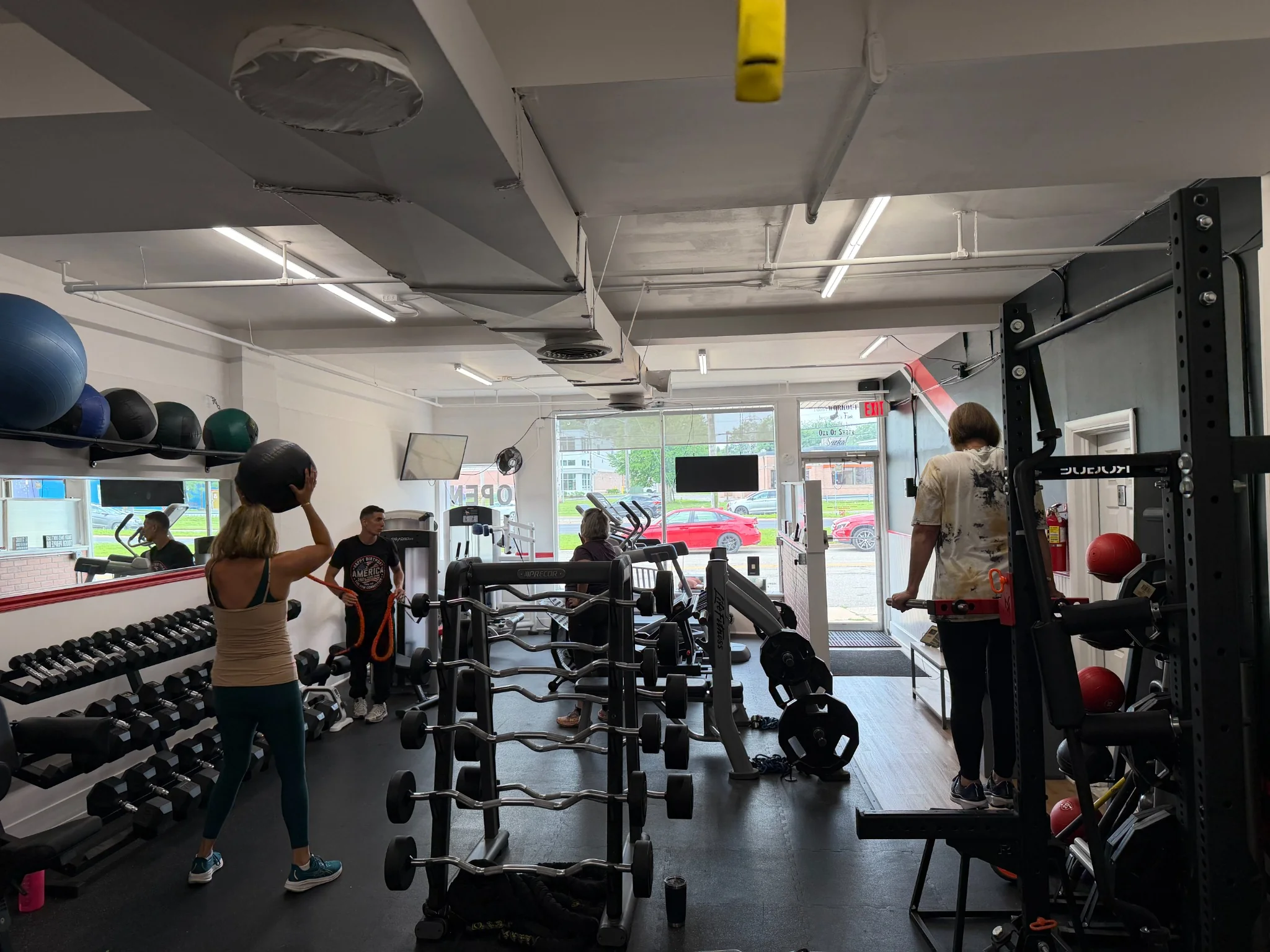 Clients and trainers on the studio floor, including a woman holding a medicine ball.