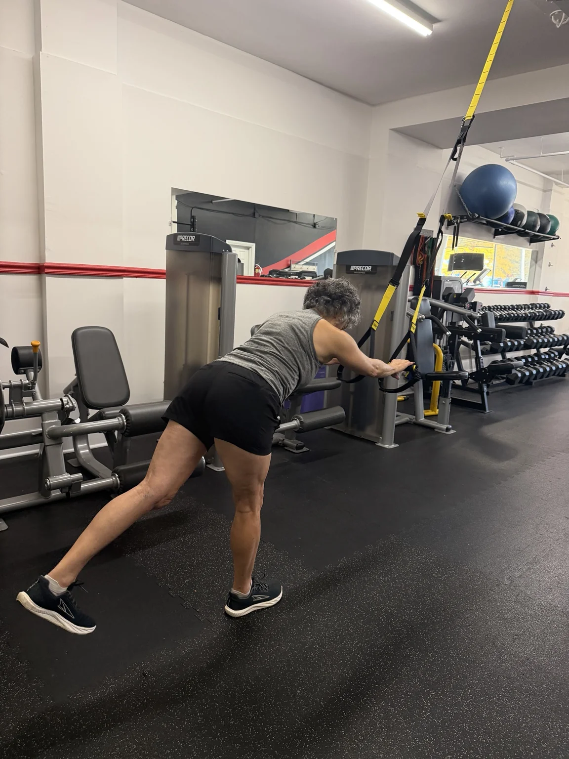 Woman using TRX suspension straps for support during a single-leg balance exercise.