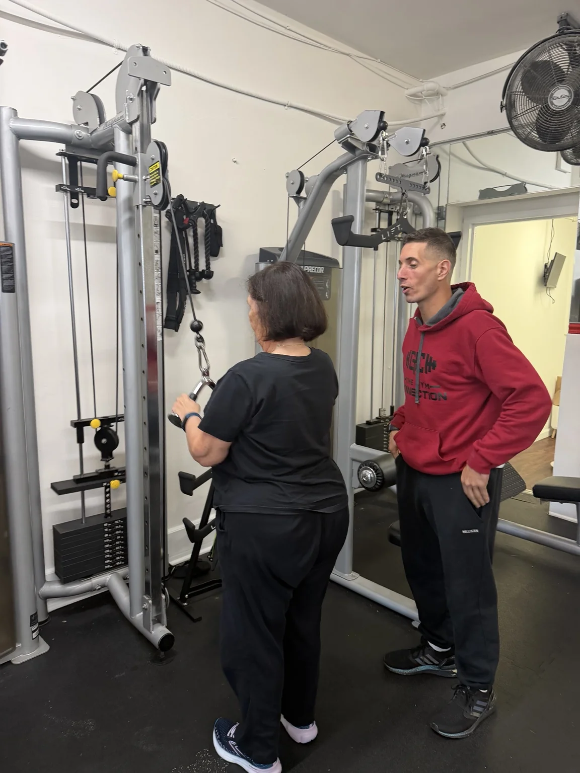 Trainer guiding a woman through a cable triceps exercise at The Gym Connection.