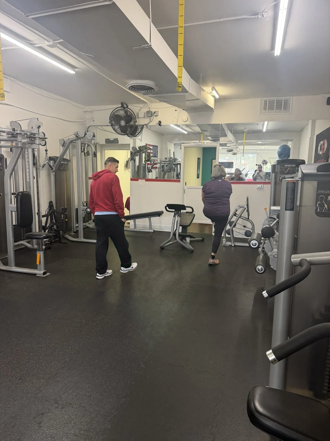 Client practicing a walking knee lift while a trainer watches from across the studio floor.